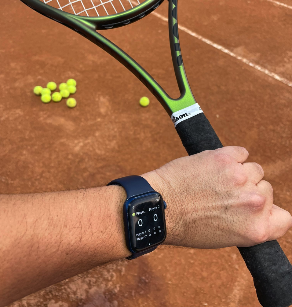 A tennis player checks their Apple Watch with the Scoremini app open, showing the current match score.